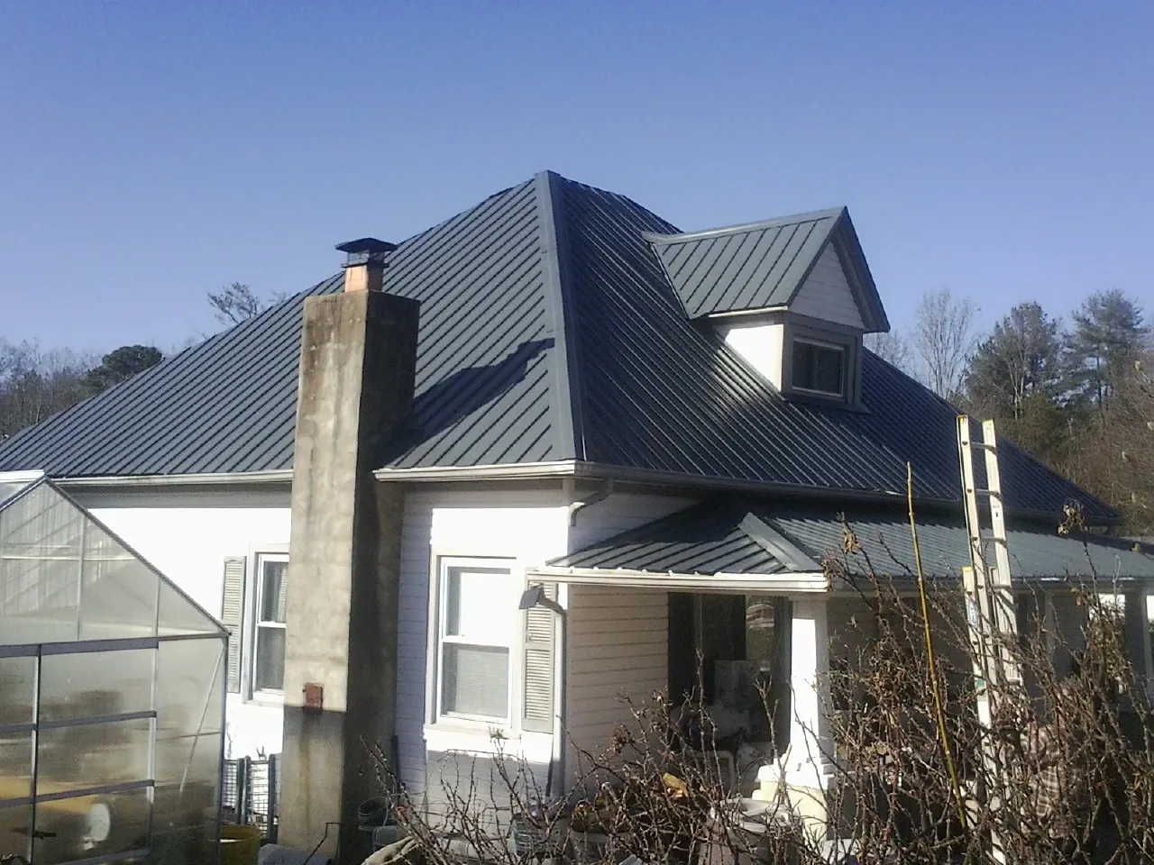 Dark blue standing seam metal roof on a white farmhouse with dormer — Slate & Tile Roof Repair by Roofing Brothers in Monitor