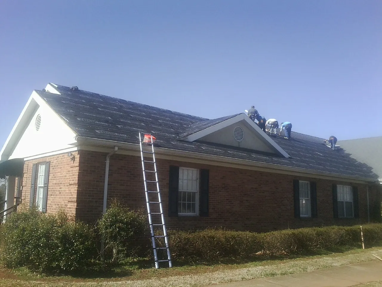 Crew tearing shingles off a brick ranch roof with a ladder set — Metal Roof Repair work by our crew in Monitor