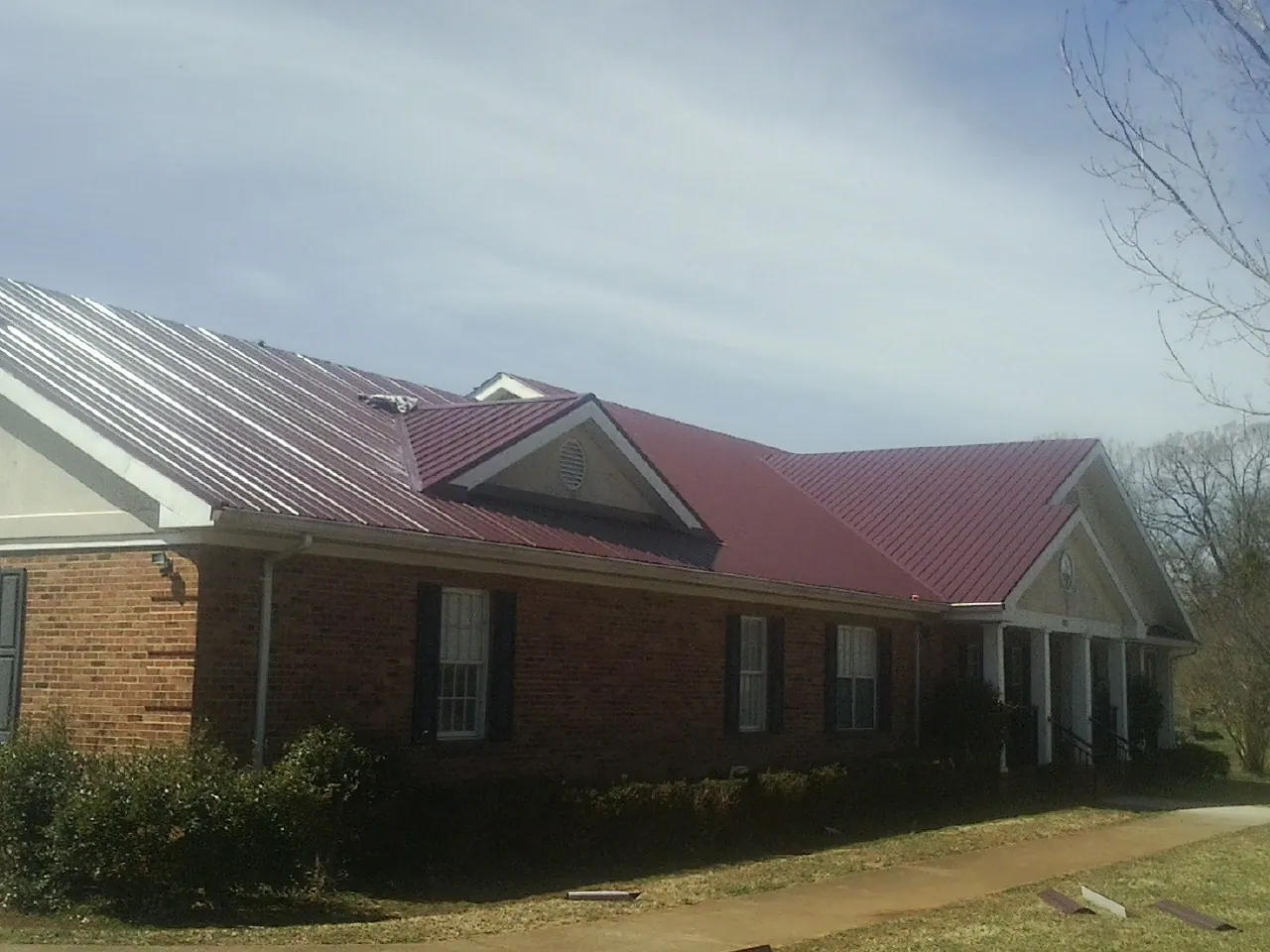 Red metal roof with gabled entries on a long brick building, from a Hail Damage Roof Repair job in Monitor