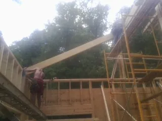 Carpenter raising a rafter beam on a new second story frame in Monitor