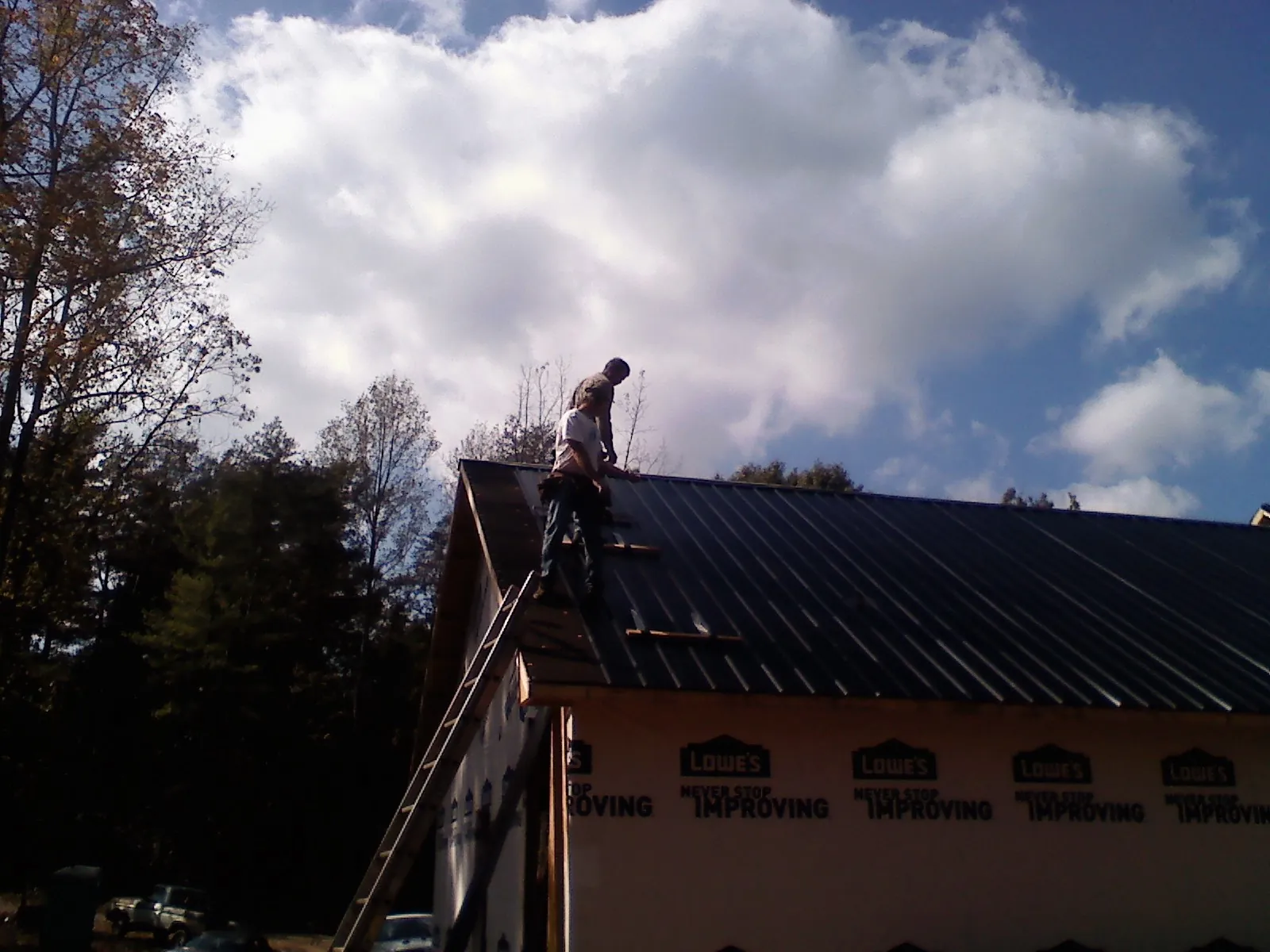 Roofer fastening dark metal panels high against a cloudy sky, from a Roof Inspection job in Monitor