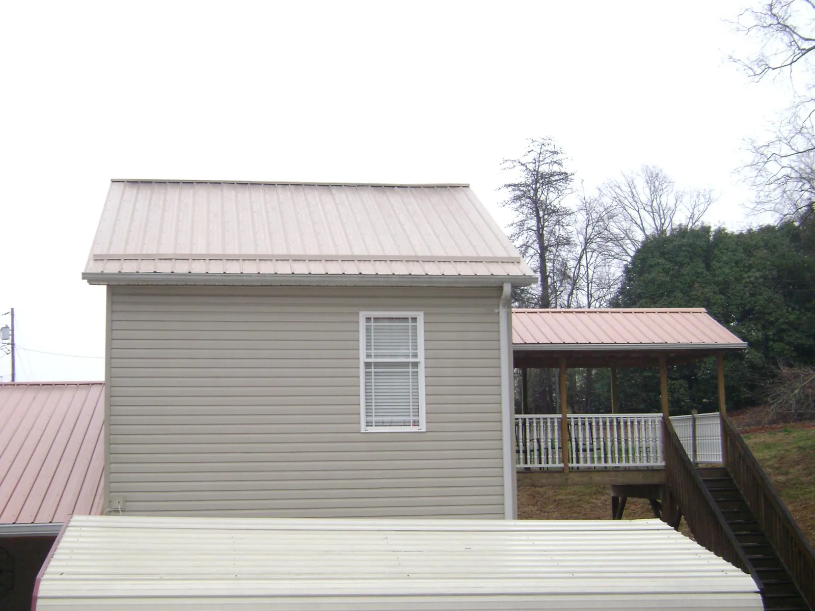 Tan metal roofs on a two story addition and attached porch, from a Roof Replacement job in Monitor
